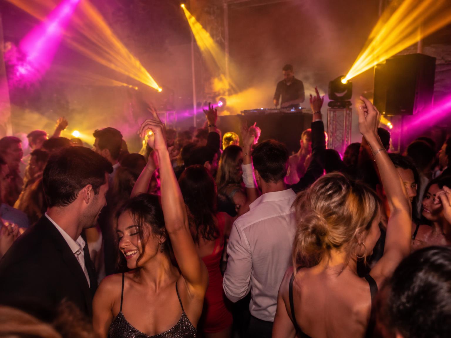 Pista de dança lotada com iluminação cênica e DJ